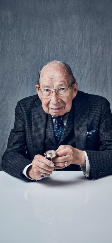 身穿灰色西装、手持万年历腕表的年长绅士