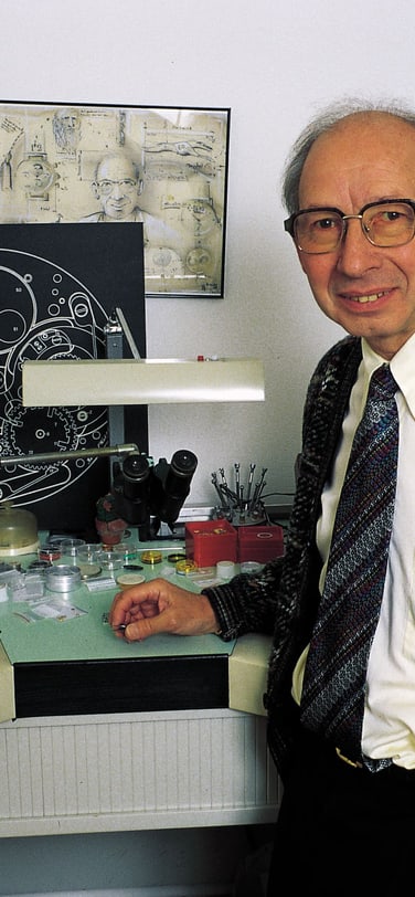 葛珞斯先生在沙夫豪森IWC万国表的工作台前，身后展示着一张机芯示意图。