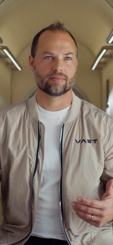 一名男性高级任务经理，身穿白色T恤和饰有Vast标志及美国国旗的米色夹克。