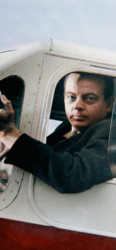 a color photo of Antoine De Saint-Exupéry sitting inside an old aircraft in the pilot seat