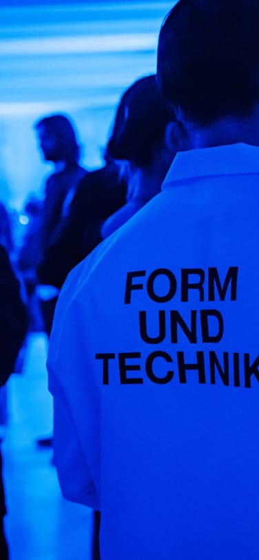 一位男士身着印有“Form und Technik”（形可依，技可循）字样的T恤，置身于蓝光氤氲的展厅。