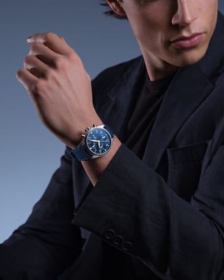 深色夹克男士手腕上佩戴蓝色表盘IWC 飞行员系列计时腕表的画面