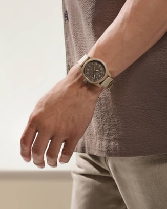 A person's arm wearing a tan, textured shirt, and a brown IWC watch with a matching band on their left wrist.