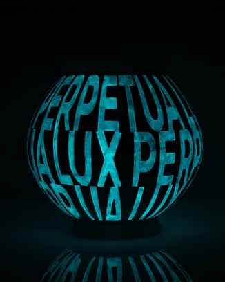 一件深色陶瓷月亮罐，以明亮蓝色Ceralume®夜光瓷釉料书写的“LUX PERPETUA”，熠熠生辉