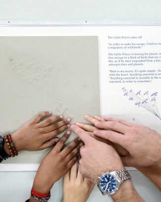 Multiple hands touching a tactile print based upon an illustration from Le Petit Prince